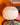 AARVEN white Sun Mask pleated paper pendant light hanging in a warm orange room, with other patterned ligh shades blurred in the background.