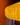 A close-up of a warm white paper lantern by AARVEN with a textured geometric Sun Mask pattern, shown against a blurred orange and dark brown background.