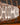 A close-up of a white paper lantern light shade by AARVEN with a black geometric sun mask pattern, shown against a blurred background with warm brown and orange tones.
