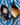 Two black ceramic spoons with fish designs on a blue and white wavy-patterned surface.