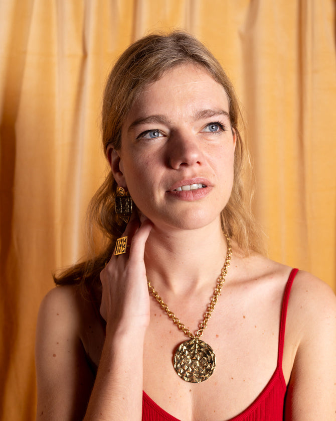 Woman wearing a red dress and gold AARVEN sunmask statement necklace against an orange curtain background