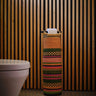 A handwoven tubular toilet roll holder with pink and green gingham design, placed against a striped wall.