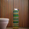 A handwoven Ghanaian toilet roll holder with a green and beige geometric pattern, displayed in a bathroom setting.