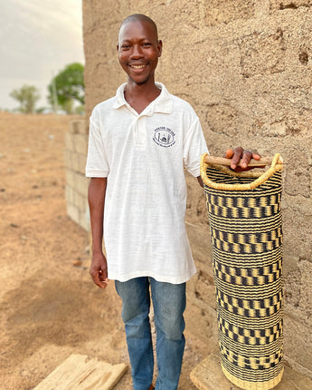 Man holding a woven toilet roll holder against a rustic wall.