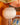 A close-up of a pleated paper lantern by AARVEN in warm off-white hanging in front of an orange wall, with other patterned hanging lanterns partially visible above and below.