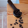 Black coffee scoop with coffee beans on a wooden surface