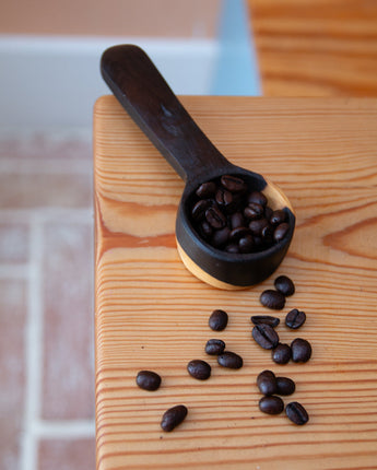 Black coffee scoop with coffee beans on a wooden surface