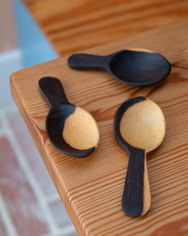 Three wooden spoons with black handles on a wooden surface.