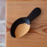 Wooden scoop with black handle on a wooden surface