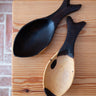 Two wooden spoons with black ends on a wooden surface.