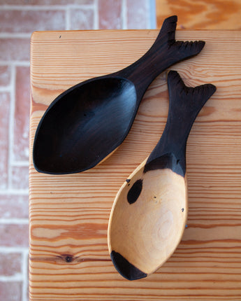 Two wooden spoons with black ends on a wooden surface.