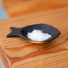 Black fish-shaped scoop with salt on a wooden surface