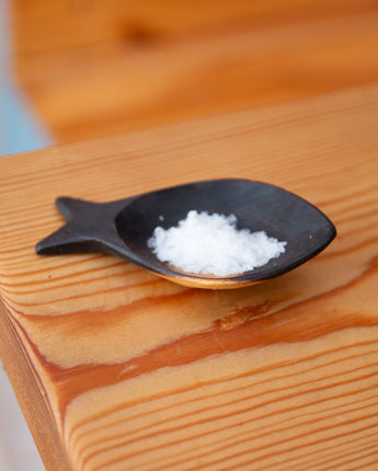 Black fish-shaped scoop with salt on a wooden surface