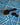 Black coffee scoop with ground coffee and whole coffee beans on a blue wavy-patterned surface