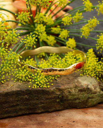Handmade gold brass bangle on a rock with greenery