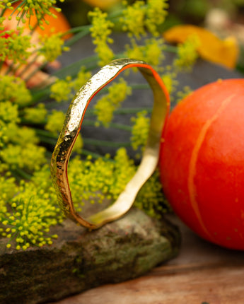 Gold bracelet on a stone surface with greenery and a pumpkin in the background