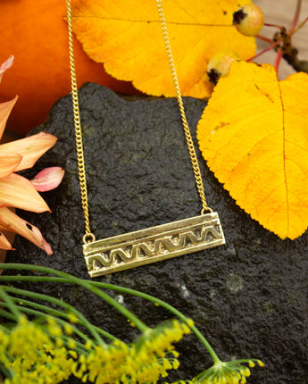 Gold necklace with a decorative pendant on a dark surface with yellow leaves and green stems.