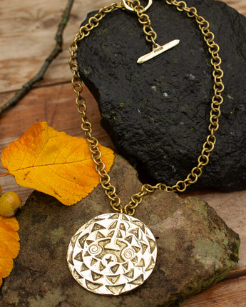 Gold necklace with a detailed pendant on a natural stone surface with autumn leaves.