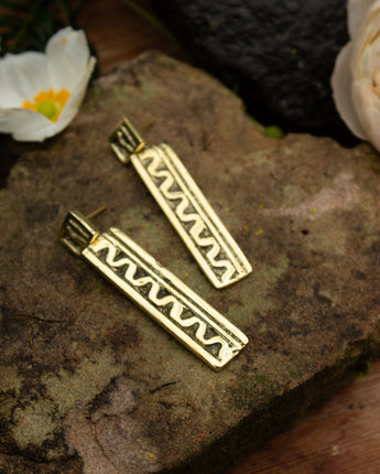 Gold bar earrings on a stone surface with flowers in the background