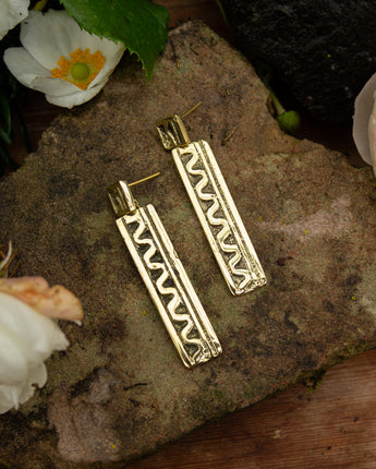 Handmade recycled brass statement earrings on a stone surface with flowers