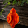 Orange paper ornament hanging against a decorative background with greenery and red berries.