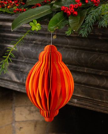 Orange paper ornament hanging against a decorative background with greenery and red berries.