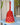 Red woven bell-shaped musical shaker rattle on a blue surface with a plant in the background