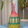 Multicolored woven rattle toy on a blue surface with plants in the background