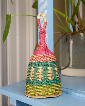 Multicolored woven rattle toy on a blue surface with plants in the background