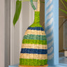Woven rattle shaker with green, blue, and beige stripes on a light blue surface.
