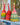 Three colourful woven rattles on a blue surface with a plant in the background.