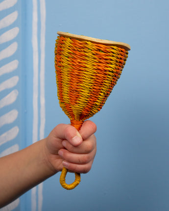 Hand holding a colourful woven rattle against a blue background