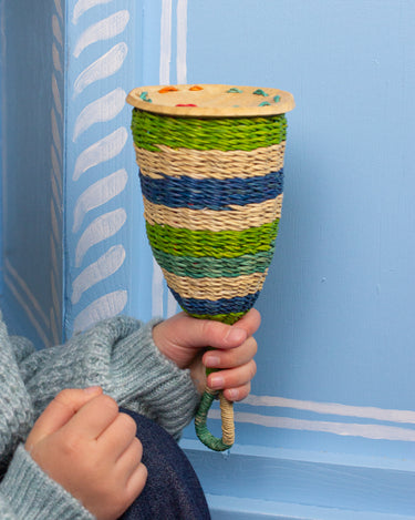 Hand holding a colourful woven rattle against a blue background