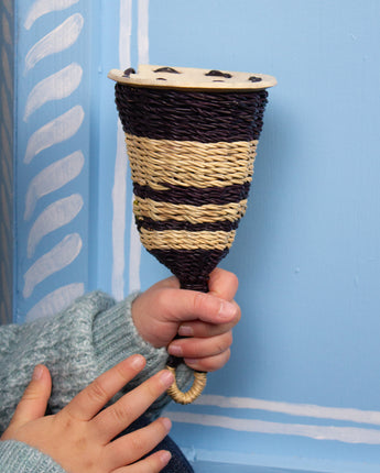 Person holding a striped woven rattle toy against a blue background