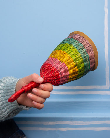 Hand holding a colourful rainbow woven rattle against a blue background