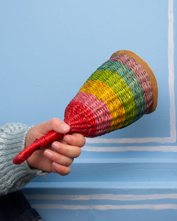 Hand holding a colourful rainbow woven rattle against a blue background