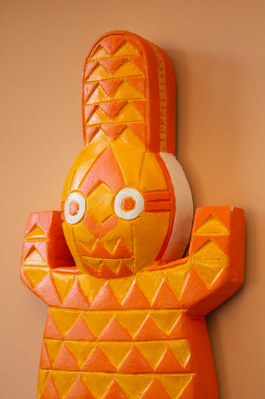 Close up of AARVEN orange geometric crocodile wall art, hand carved by artisans in Ghana, on a peach background