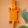 Orange geometric crocodile wall art, hand carved in Ghana, with a plant in the foreground on a peach background