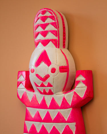Hand carved fluoro pink and white geometric pattern Ghanaian crocodile mask. Close up on peach wall.