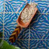 Terracotta scoop filled with oatmeal against a blue wavy tile background