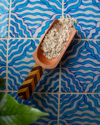 Terracotta scoop filled with oatmeal against a blue wavy tile background