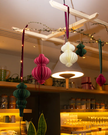 Decorative hanging recycled paper ornaments in a store setting with shelves and products in the background.