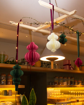 Decorative hanging recycled paper ornaments in a store setting with shelves and products in the background.
