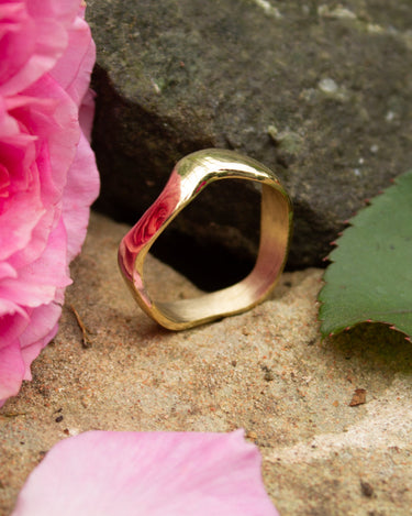 Gold ring on a stone surface with pink petals and a pink flower.