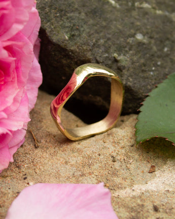 Gold ring on a stone surface with pink petals and a pink flower.