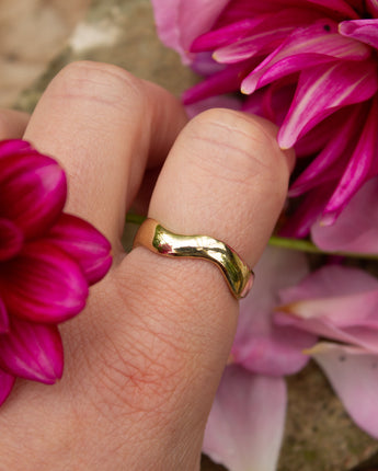 Gold ring on a finger with pink flowers in the background