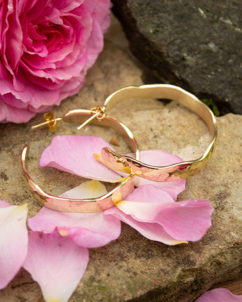 Gold hoop earrings on pink flower petals with a pink rose in the background