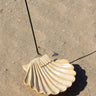 Shell incense holder by AARVEN with an incense stick on a sandy surface