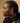 A woman with braided hair wearing the gold tone hoop earrings, set against a yellow background.