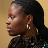 A woman with braided hair wearing the gold tone hoop earrings, set against a yellow background.